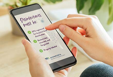 Person holding a phone looking at a social media animation for the Minnesota Board of Cosmetology highlighting the requirements for disinfectants in a salon