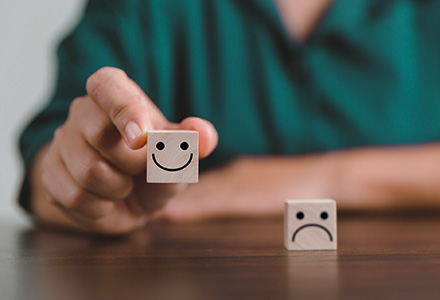 Person holding a block with a smiley face on it. Frowny face block sits on table.