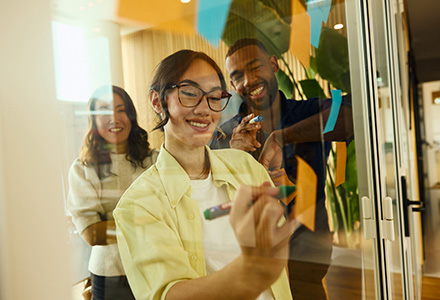 Work colleagues writing on sticky notes on a glass wall