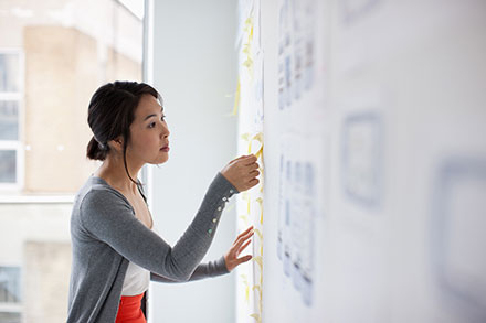 Woman putting Post-it notes on a whiteboard full of content