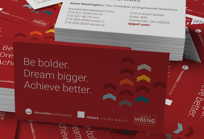 Photo of a stack of business cards for APG Office Furnishings with the tagline: Be bolder. Dream bigger. Achieve better.